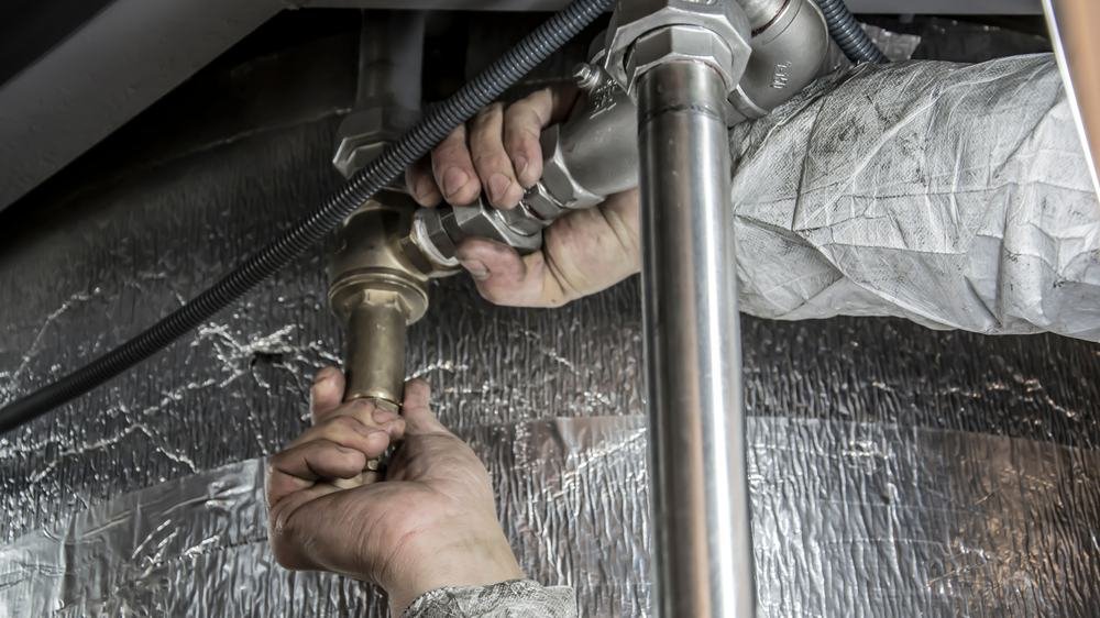 Réparation d'une fuite d'eau sur un raccord de plomberie, gros plan sur les mains d'un plombier